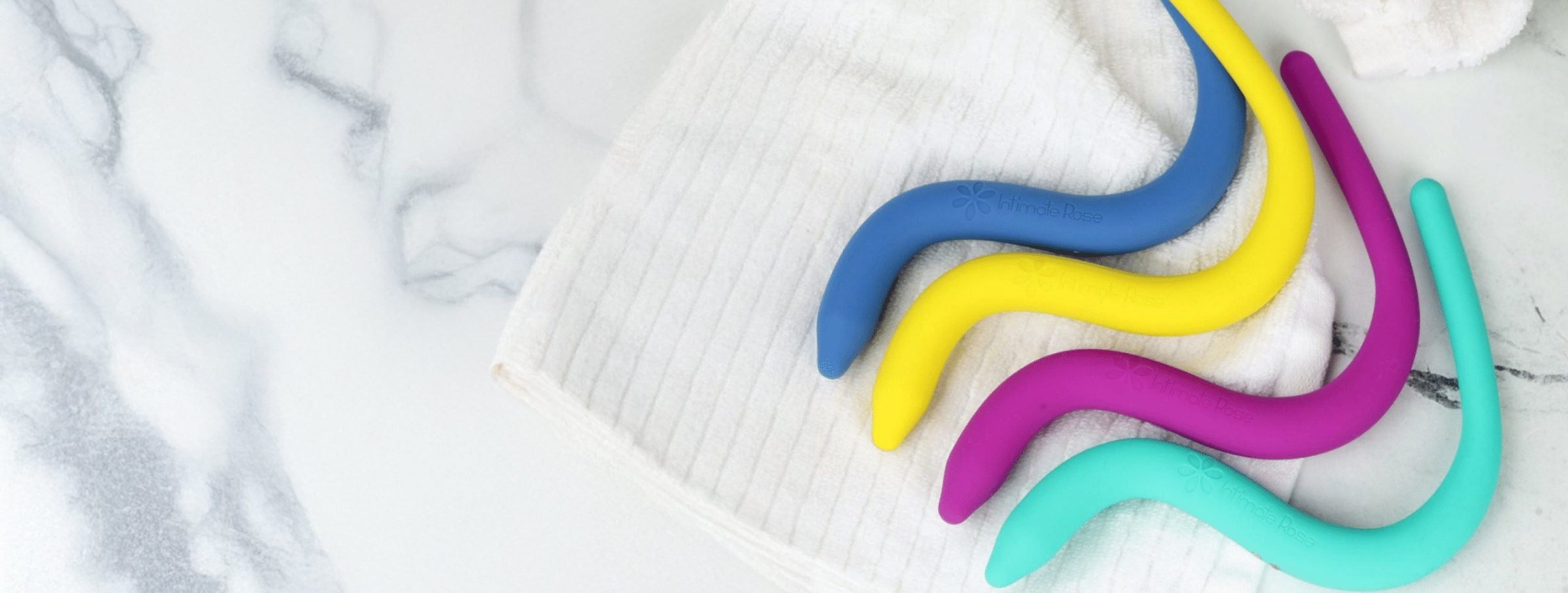 Four pelvic wands in blue, yellow, magenta and teal resting on a folded white towel on marble.
